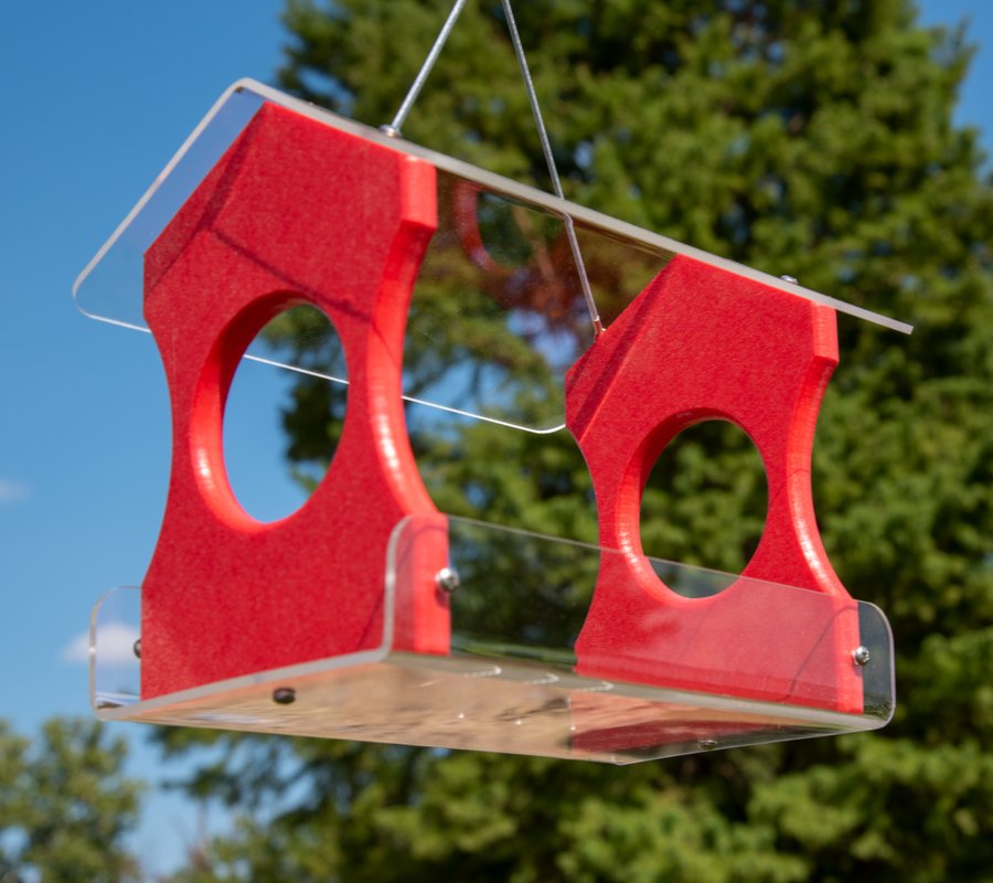 JCS Wildlife Recycled Poly Lumber Hanging Bird Feeder in bright red with space for 3 cups of seed, outdoors against green trees and blue sky.