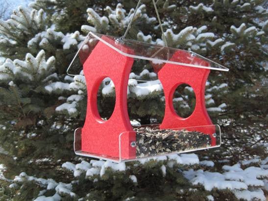 JCS Wildlife Recycled Poly Lumber Hanging Bird Feeder in vibrant red with black oil sunflower seed, hanging in snow-covered pine trees.