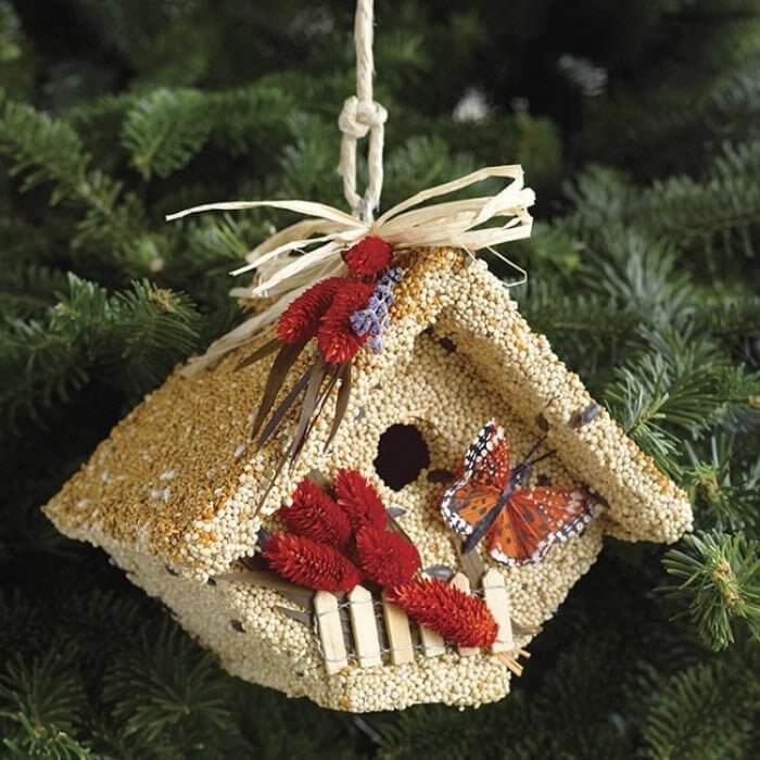 Wooden birdhouse covered in bird seed with decorative butterflies and flowers, perfect for backyard birds and bird-lovers.