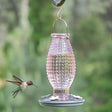 Vintage-style cranberry hobnail glass hummingbird feeder with 16 oz nectar capacity and 4 feeding ports, attracting hovering hummingbird