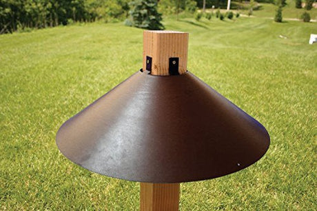 Woodlink 22" bronze wrap around baffle mounted on 4x4 post protecting against squirrels and predators in a green outdoor setting.