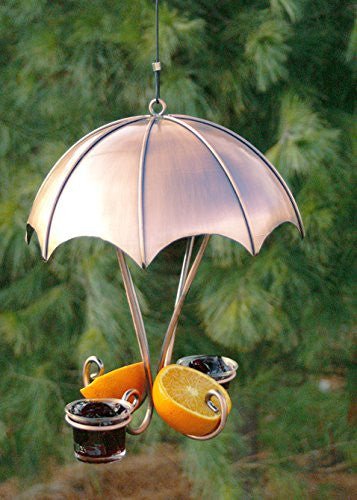 Metal garden art hummingbird feeder featuring a copper umbrella design with two juicy orange slices and dark red jelly accents hanging outdoors against a lush green background