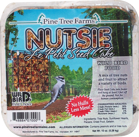 Pine Tree Farms Nutsie Le Petit Seed Cake package shows a downy woodpecker in a woodland setting with a bird feeder containing colorful nuts and seeds near tall trees
