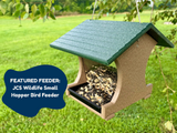 JCS Wildlife Small Hopper Bird Feeder photo showing a dark green roof tan body and a mix of birdseed in a backyard setting with green grass
